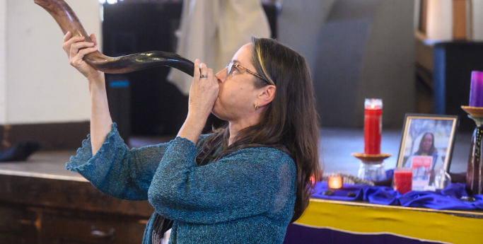 image of a woman blowing a shofar with a shrine in the background.