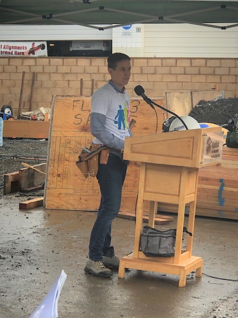 Image of a person talking at a lectern outside at a house buildling 