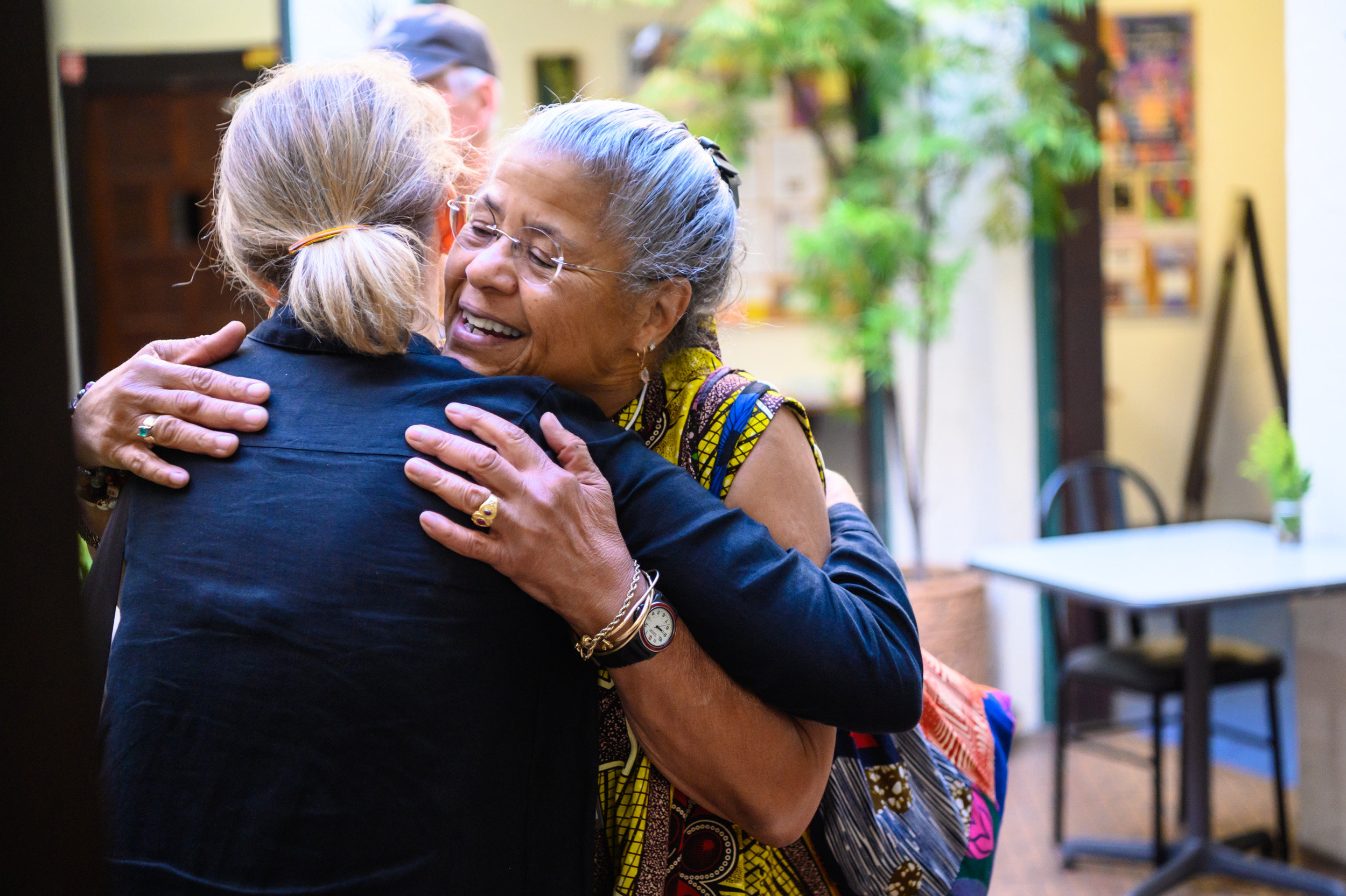 Former Board President Sister Marie Taylor faces the camera and hugs Vice President Vanna Whitney. She has a warm smile on her face.