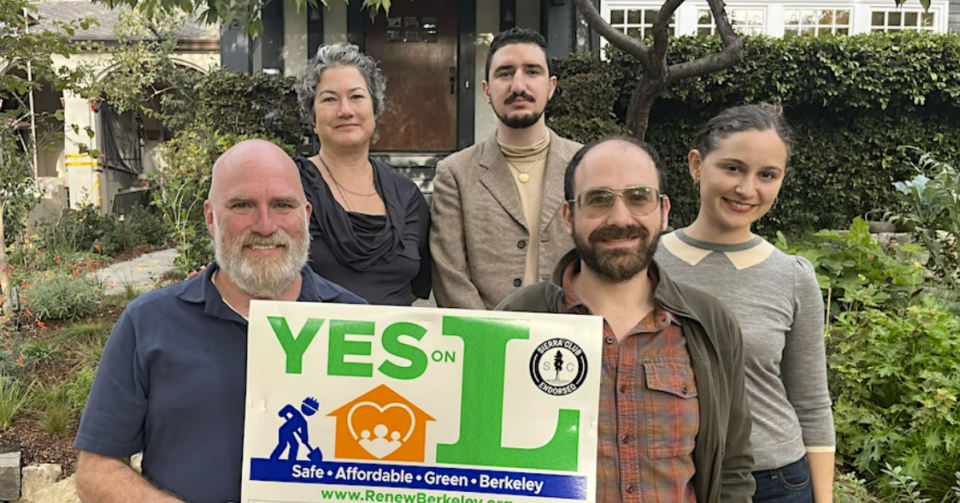 A group of people smile and hold a Yes on L sign outside of their home.