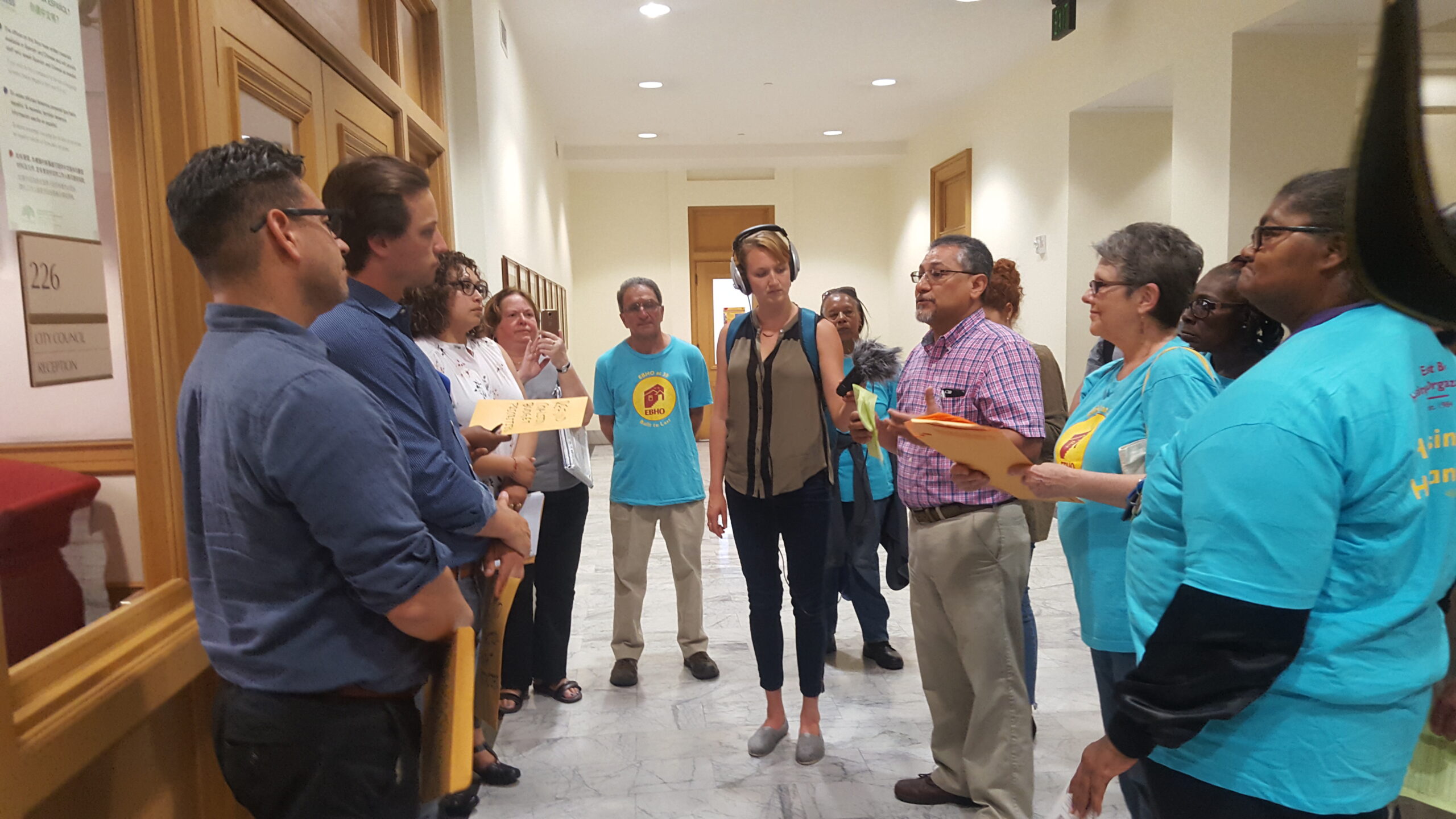 Advocates in teal EBHO shirts stand in a circle and talk to legislative aides at Oakland City Hall.